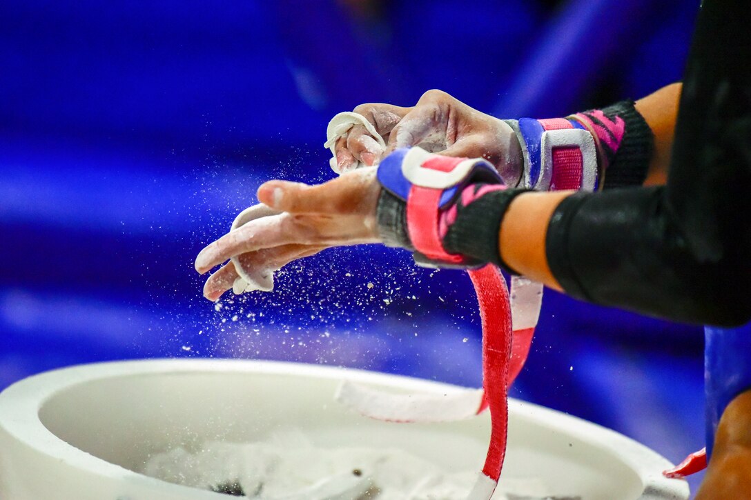 Powdered chalk falls off the hands of a gymnast over a white bowl.