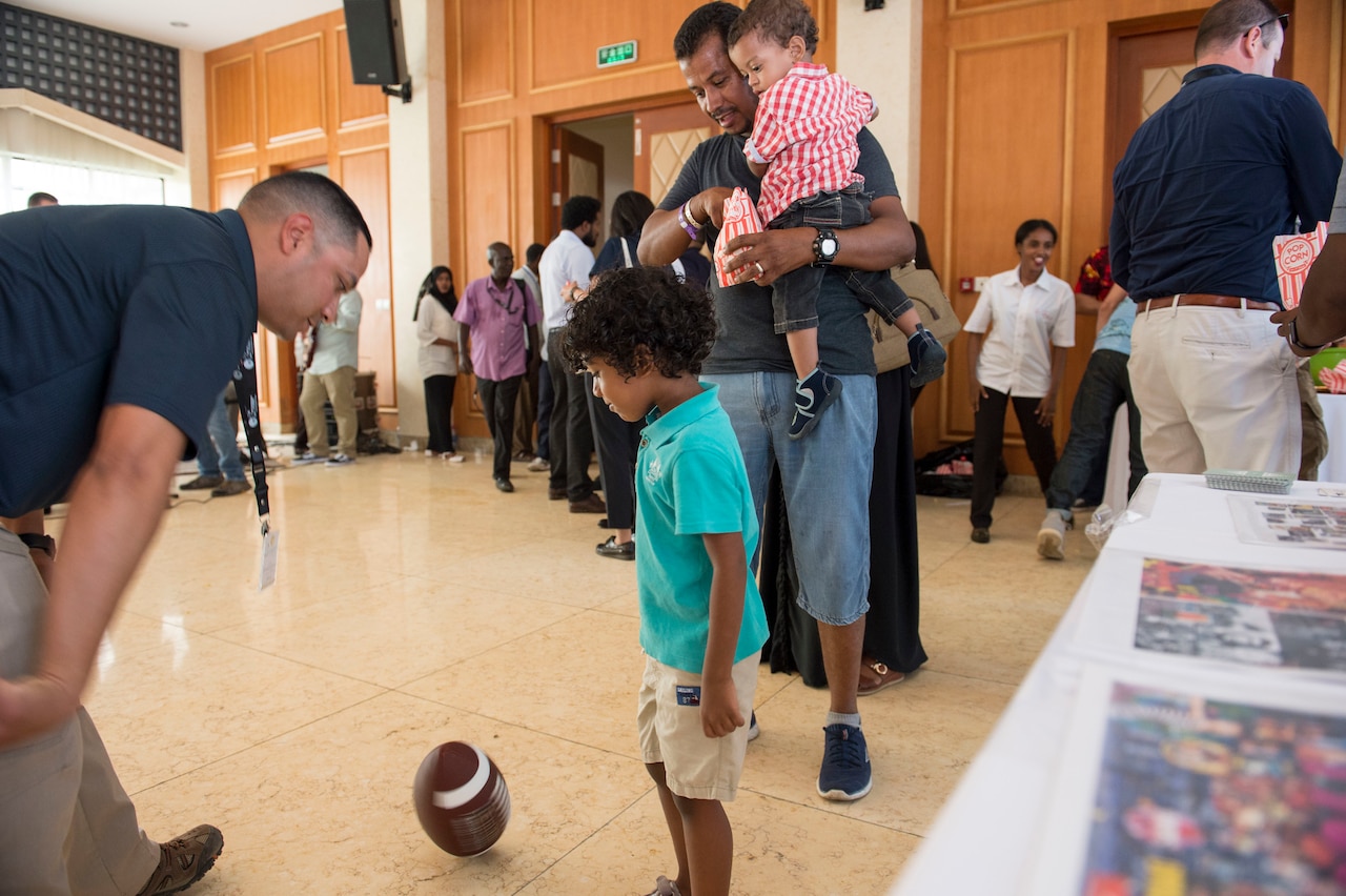 A child plays with a football next to a man at a trade fair