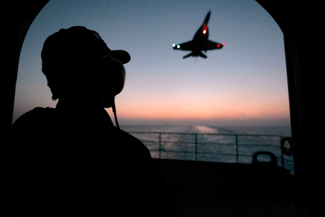 A sailor looks out over the sea as a plane flies.