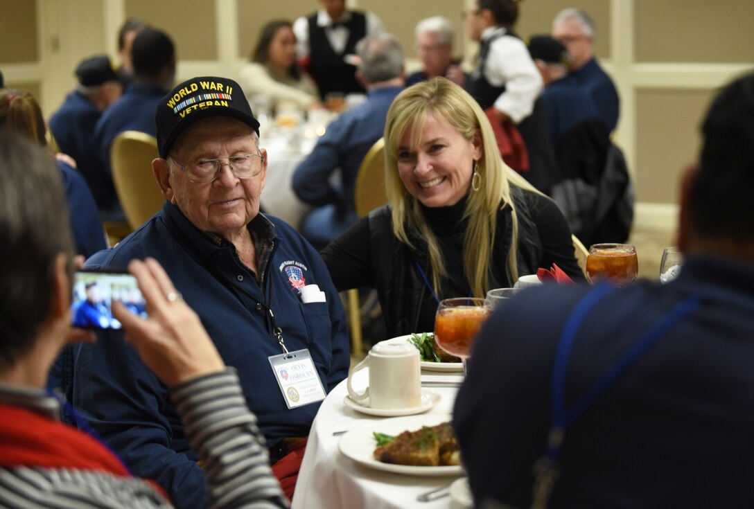 A woman takes a photo of a veteran and another woman at a dinner table.