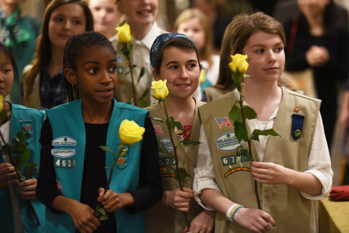 Girl Scouts holding yellow roses stand in a group.