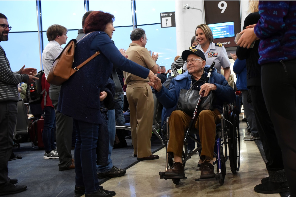 A woman shakes hands with a veteran in a wheelchair at an airport terminal.