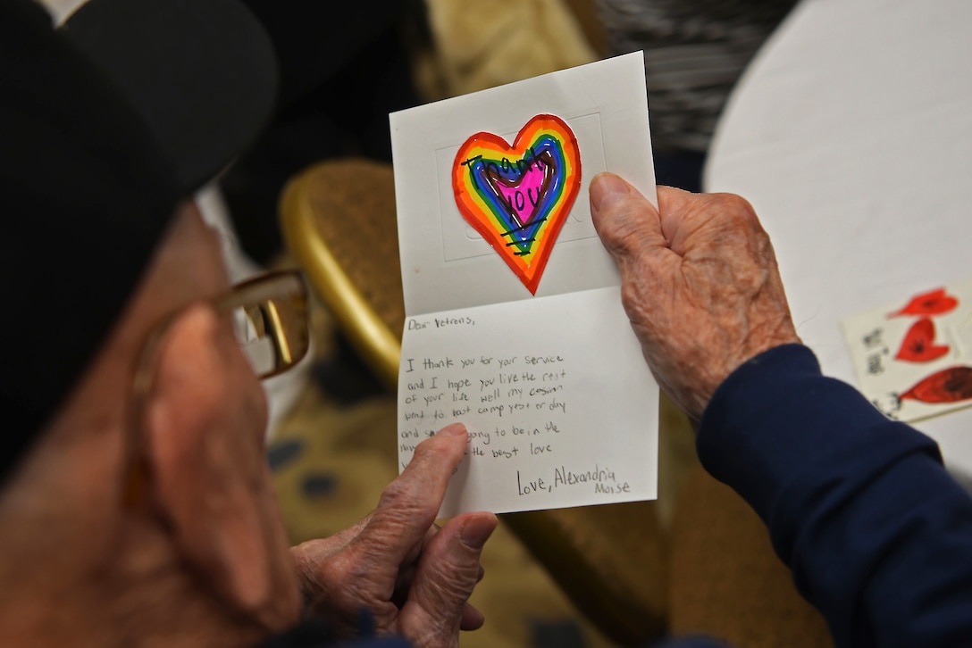 A veteran holds up a card with a child's drawing of a heart in rainbow colors.