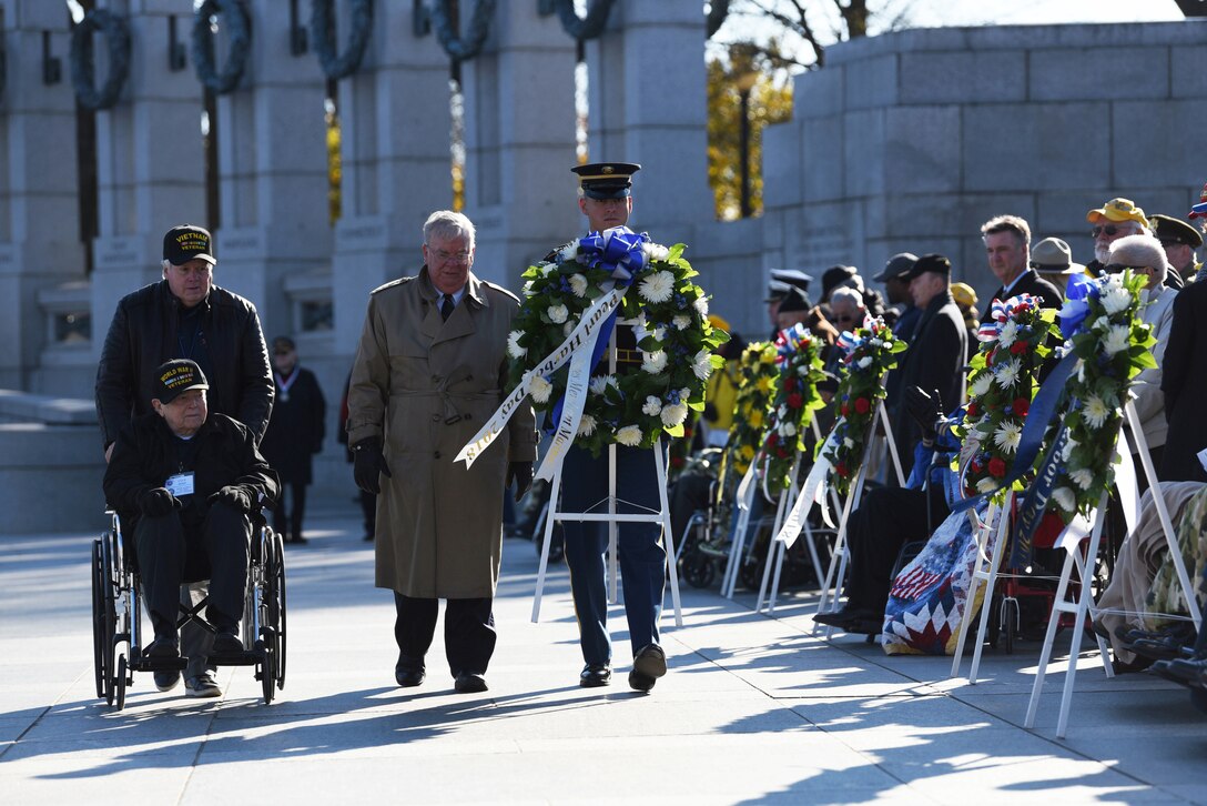 Veterans proceed with a service member carrying a wreath past onlookers during a ceremony.