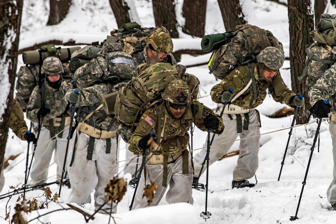 A group of soldiers hike uphill through snowy terrain.