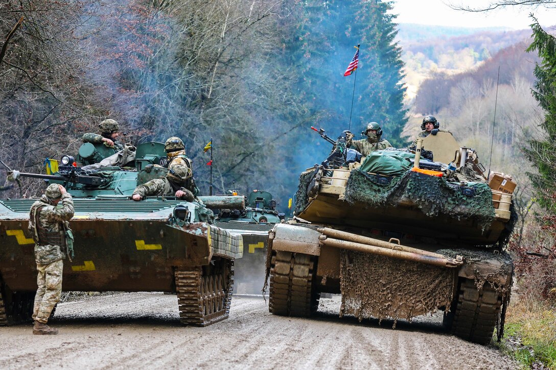 A tank carrying soldiers pulls up next to another.