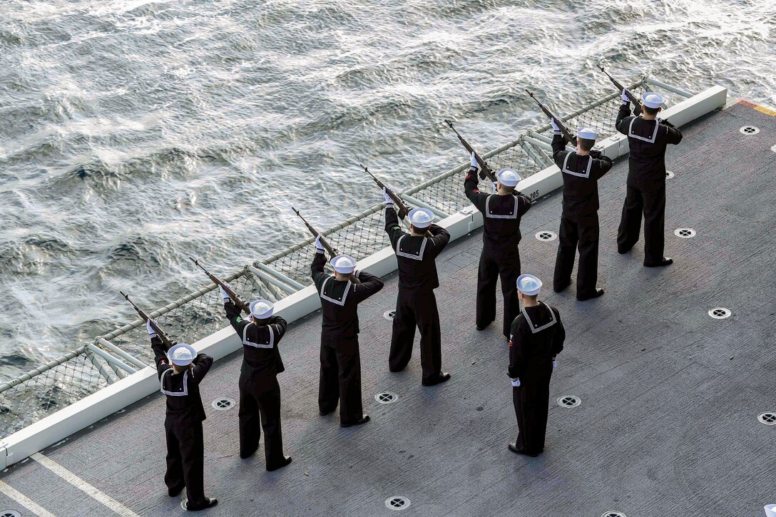 Sailors line up and fire rifles into the open sea.