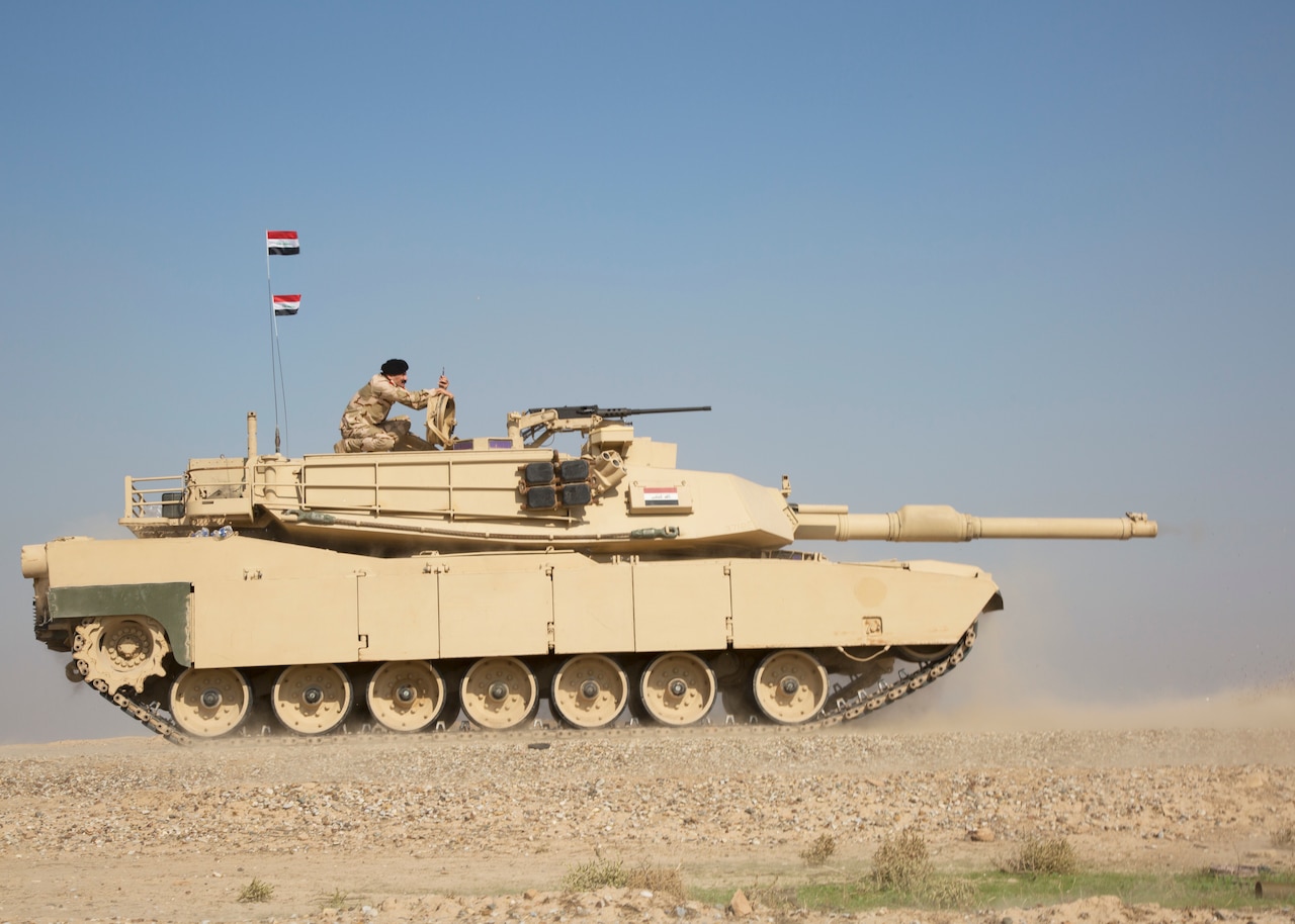 Iraqi soldier watches exercise from top of tank.