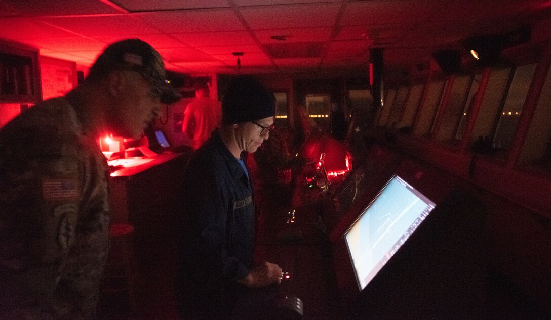 U.S. Army Chief Warrant Officer 2 Alpan Risvanoglu, 335th Transportation Detachment, 10th Trans. Battalion, 7th Trans. Brigade (Expeditionary) second mate, and Chief Warrant Officer 3 Matthey Godfrey, detachment vessel master, observe digital navigation information on the bridge of the U.S. Army Logistical Support Vessel at the port of Joint Expeditionary Base Little Creek-Fort Story, Virginia, Nov. 5, 2018. The bridge of the LSV is lit with only red lighting to keep the crew’s eyes adapted to the night. (U.S. Army photo by Spc. Travis Teate)