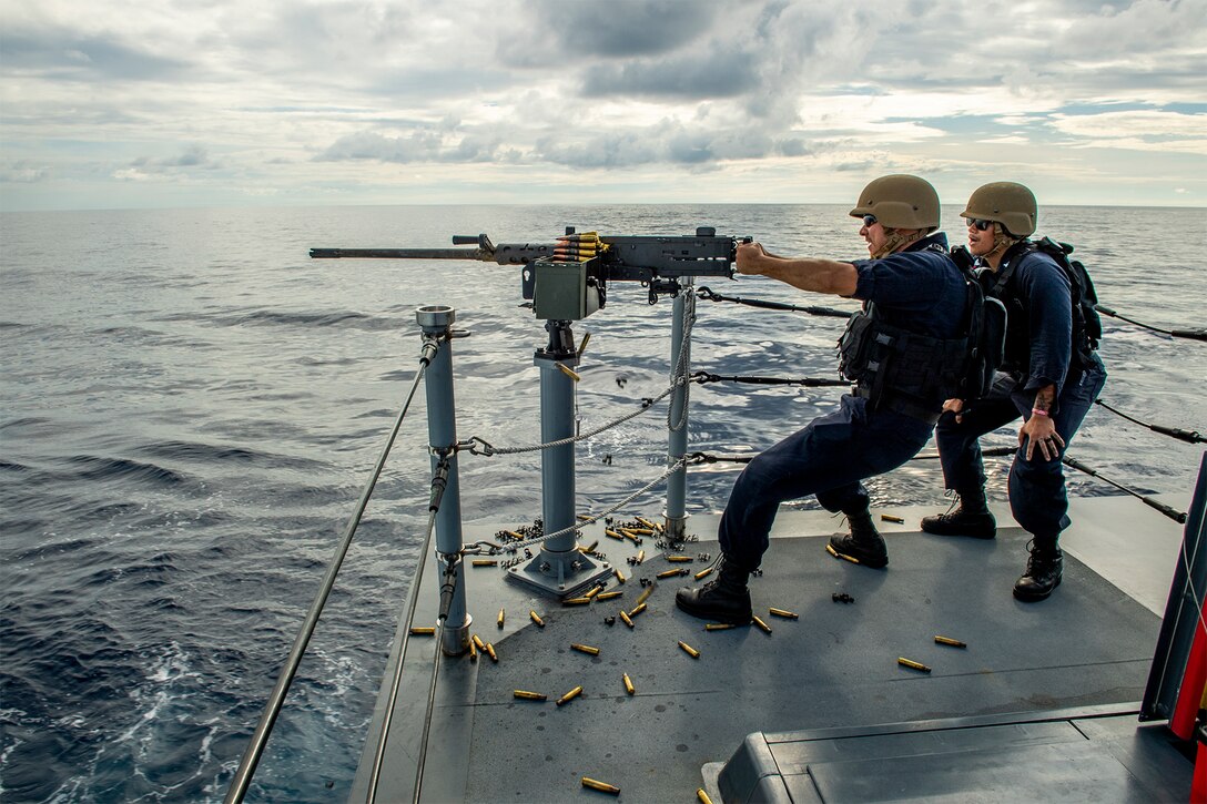 A sailor shoots a machine gun on a ship during a training exercise.