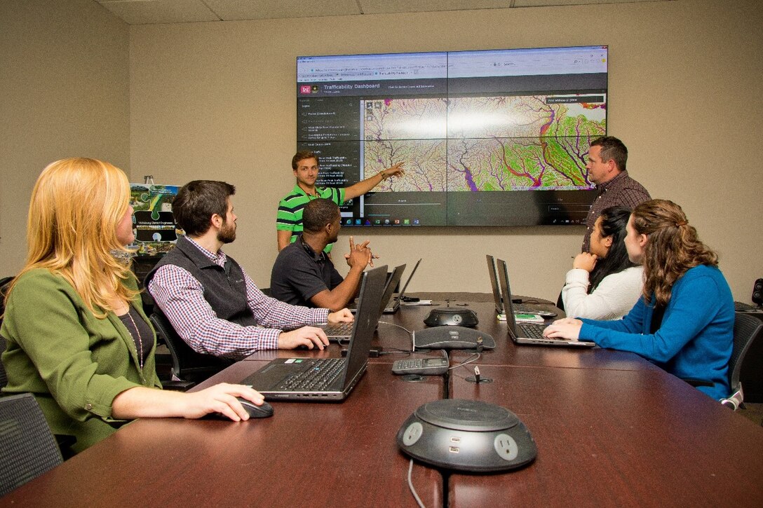 Jimmie Elliott, hydraulic engineer with the U.S. Army Corps of Engineers -Vicksburg District (MVK), addresses members of the Modeling, Mapping, and Consequences Production Center (MMC), at MVK, Nov. 27, 2018. In the background is the trafficability dashboard produced by the MMC. (USACE photo by Jared Eastman)