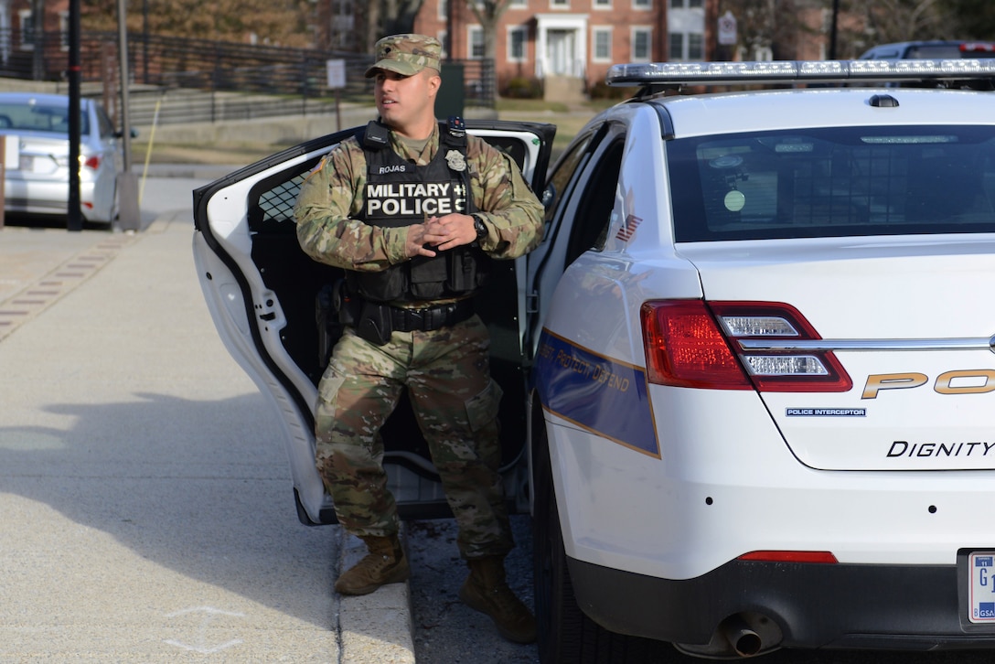 Specialist Rojas stands by his police car.