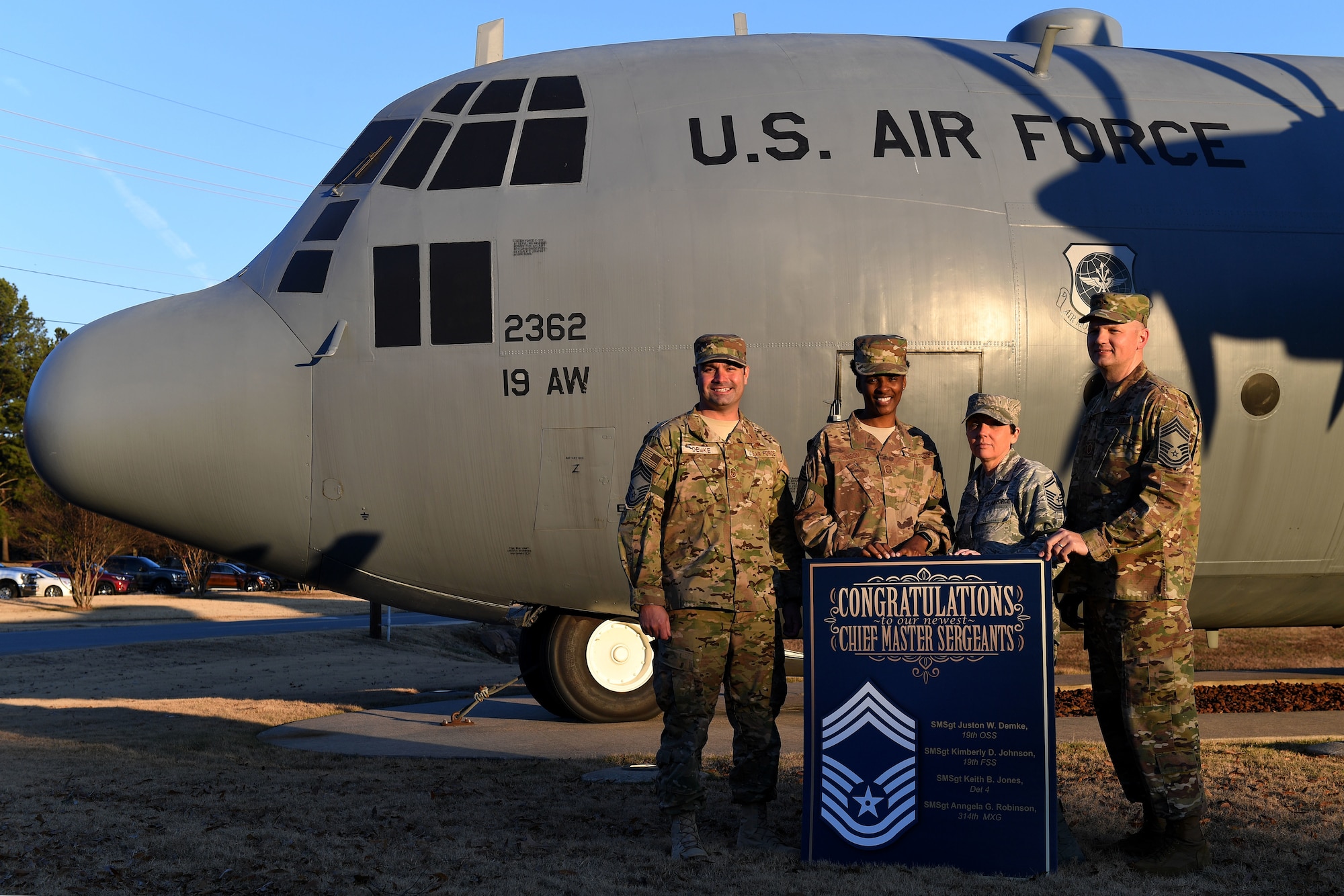 Four people in camouflage uniforms stand in front of a big gray plane with US Air Force on it.