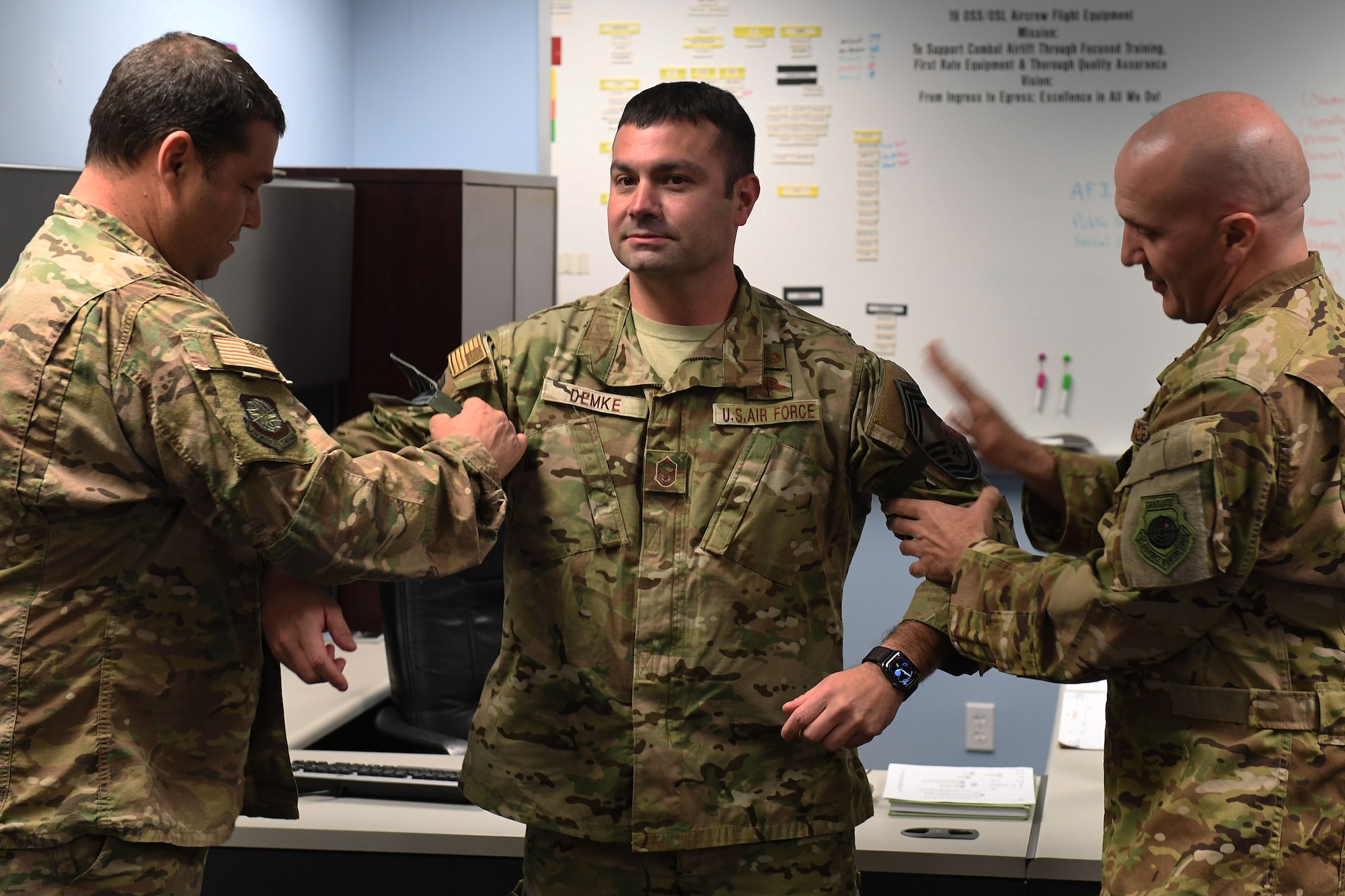 Two male Air Force Officers in camouflage put rank on another Air Force male.