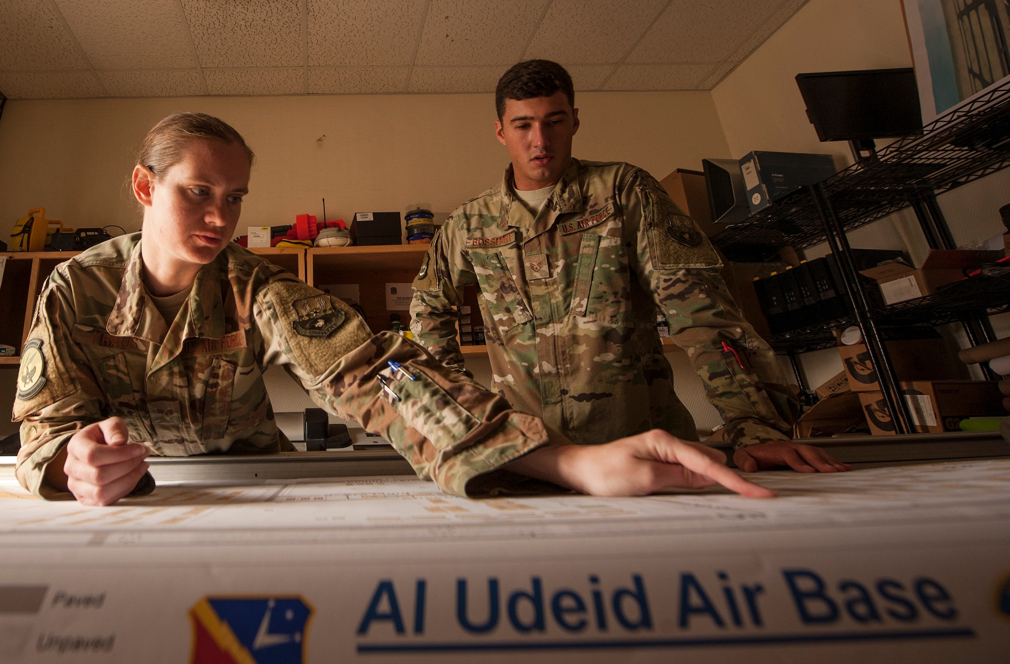 Senior Airman Jessica Kraus, 379th Expeditionary Civil Engineer Squadron geobase technician, and Staff Sgt. Arich Bosshart, 379th ECES geobase NCO in charge, look over an installation map prior to trimming its edges Dec. 11, 2018, at Al Udeid Air Base, Qatar. Bosshart and Kraus are responsible for creating and updating installation maps with the use of geospatial information system equipment and automated computer-aided design and drafting software. They also provide surveying support to construction that occurs on Al Udeid. (U.S. Air Force photo by Tech. Sgt. Christopher Hubenthal)