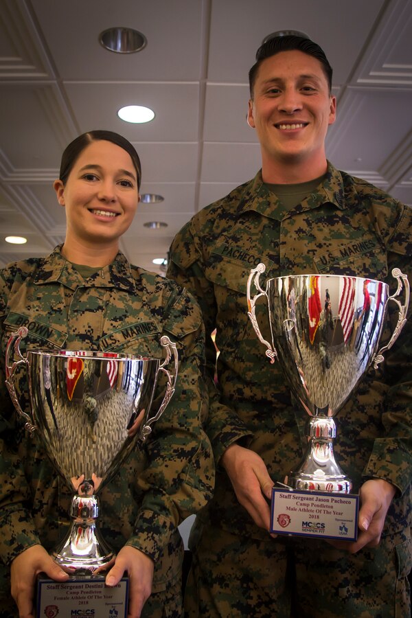 U.S. Marine Corps Staff Sgt. Destini Brown, left, transmissions chief, Combat Logistics Regiment 1, 1st Marine Logistics Group, and Staff Sgt. Jason Pacheco, right, recovering service member, Wounded Warrior Battalion West, Marine Corps Installations West, are presented with trophies after being recognized as the Marine Corps Base (MCB) Camp Pendleton Male and Female Athletes of the Year at MCB Camp Pendleton, California, Dec. 11, 2018. (U.S. Marine Corps photo by Cpl. Juan Bustos)