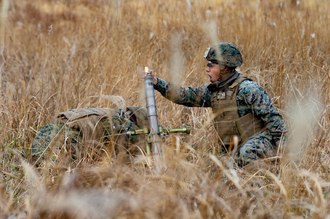 Two Marines prepare to fire a mortar in a field.
