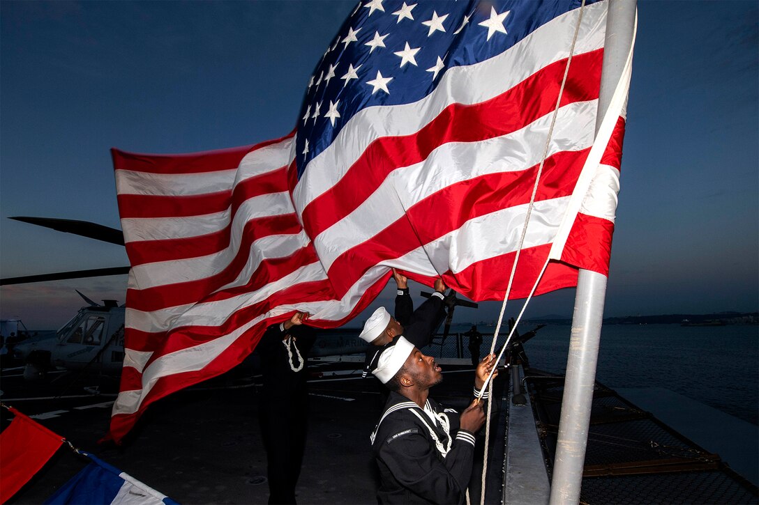 A sailor raises the American flag during a burial-at-sea ceremony.