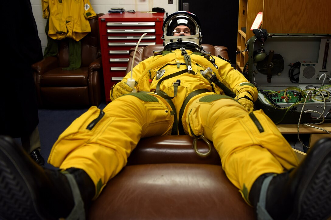 An Air Force pilot demonstrates a yellow pressure suit while lying on his back.