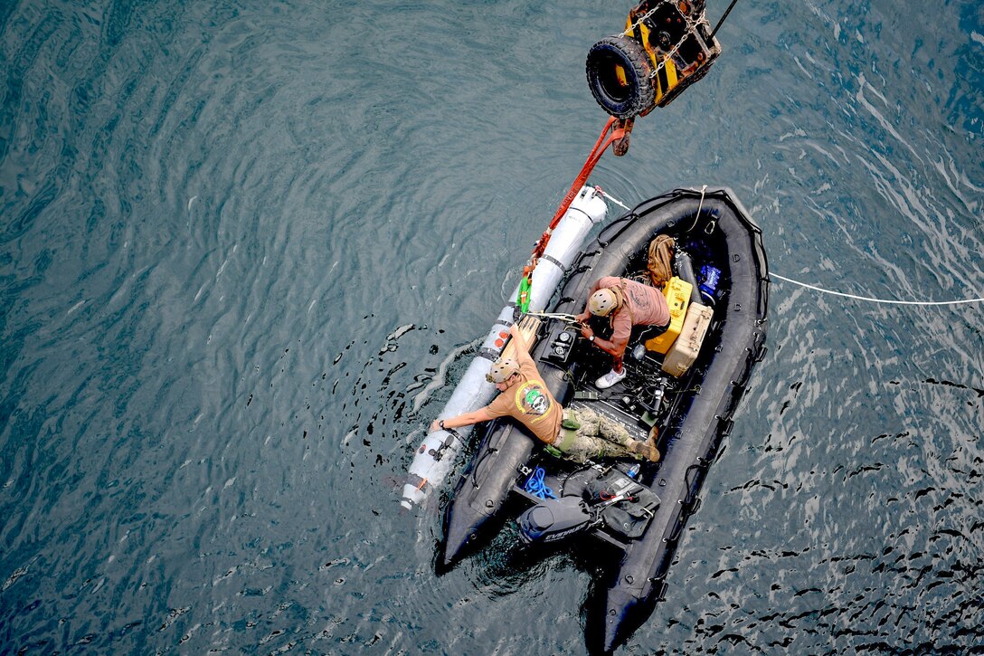 Two sailors in a rubber boat prep an underwater craft.