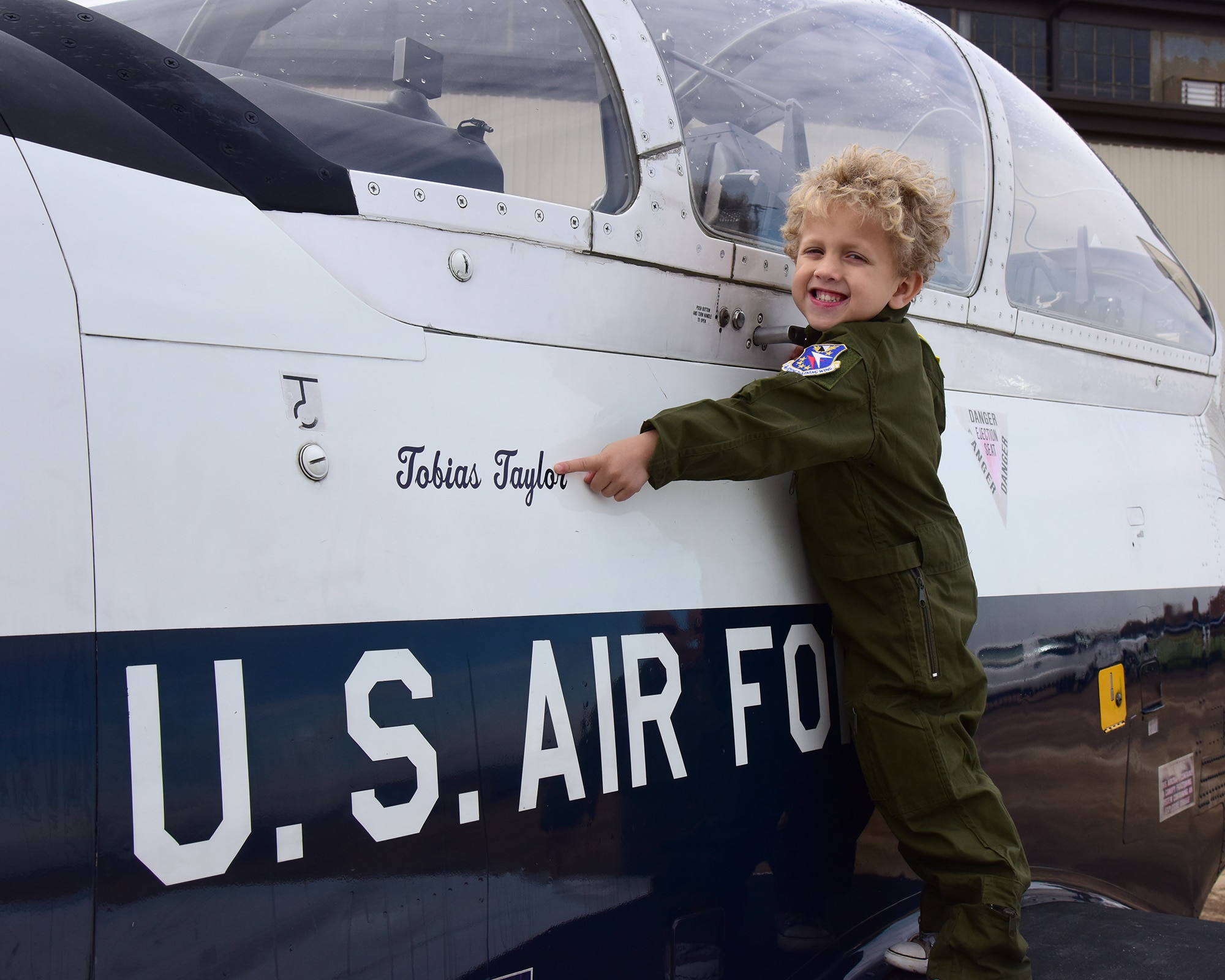 Tobias Taylor, Pilot for a Day, points to his name on a T-6 Texan II on the flight line, Dec. 6, 2018, at Columbus Air Force Base, Mississippi. While unable to actually fly in an aircraft, Tobias and his family enjoyed many aspects of Columbus AFB including displays of all three 14th Flying Training Wing training aircraft, a personalized tour of the fire department, time in the T-6 flight simulator, and more. (U.S. Air Force photo by Elizabeth Owens)