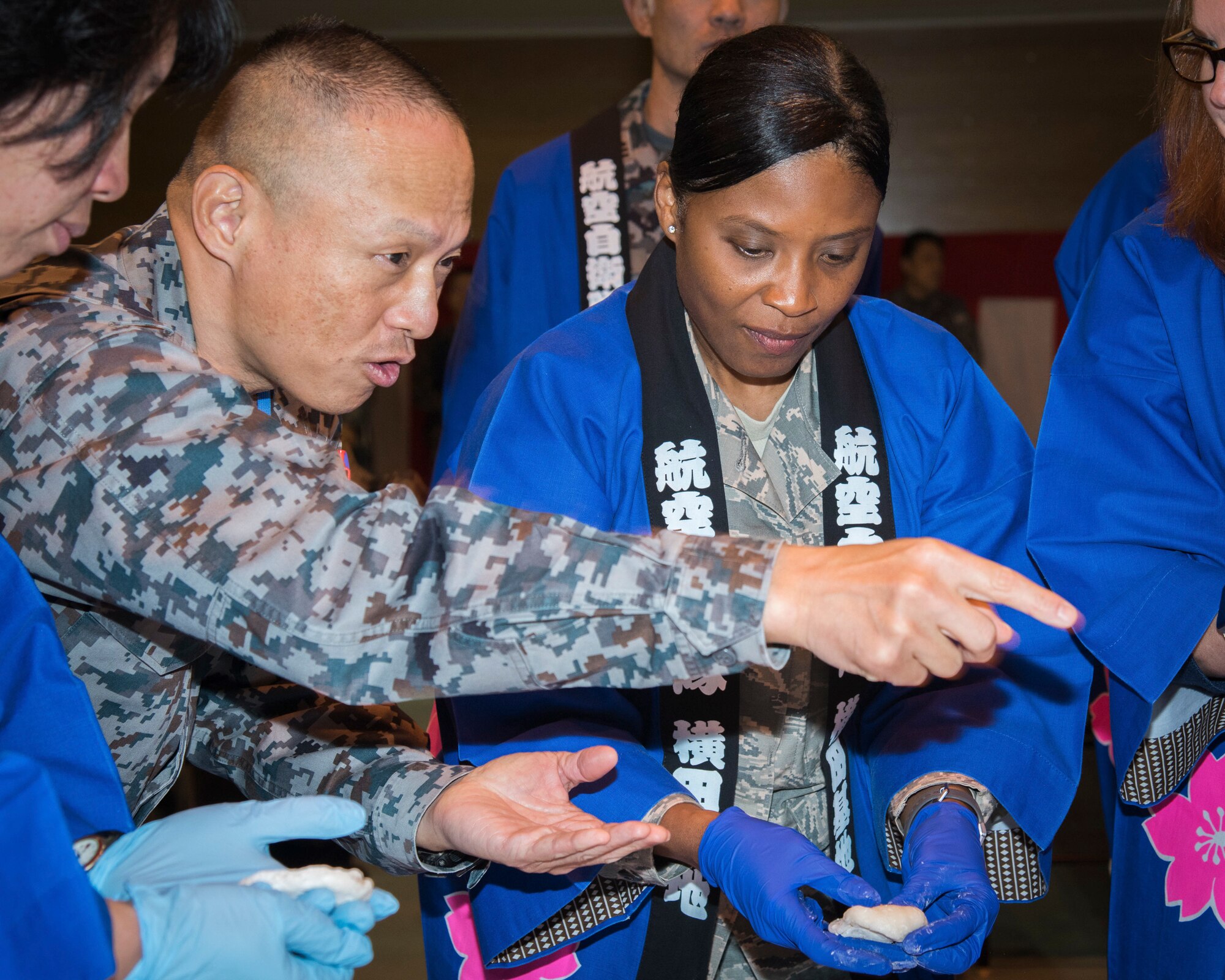 Japan Air Self-Defense Force Lt.Col. Ryuji Yamawaki, Air Base Support Squadron commander, teaches Col. Tanya J. Anderson, 374th Mission Support Group commander, how to form rice cake into a flattened round shape during pounding rice event hosted by Japan Air Self-Defense Force at Yokota Air Base, Japan, Dec. 12, 2018.