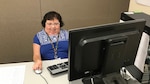 Woman sits behind desk working on computer.