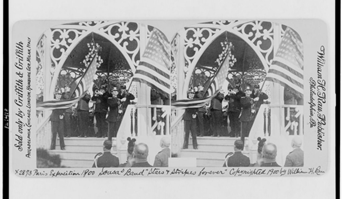 An old photo of the John Philip Sousa Band playing while American flags wave.