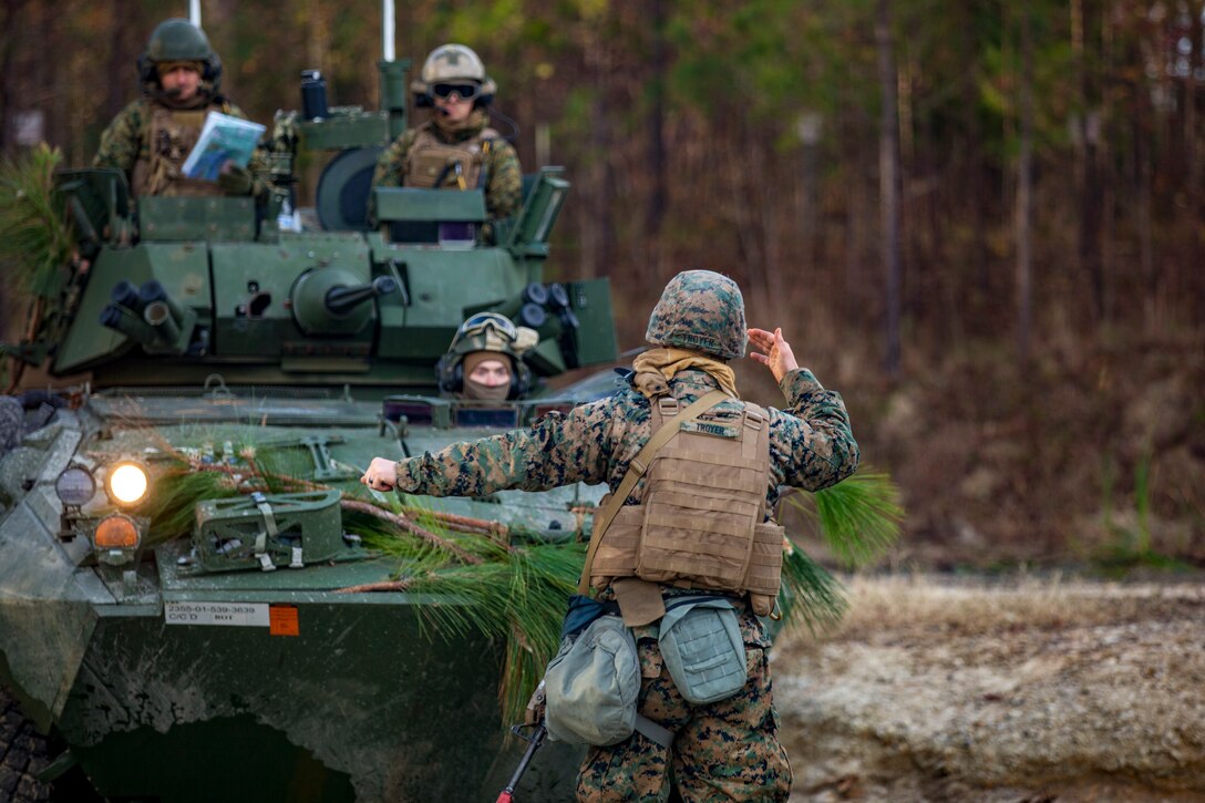 A Marine uses hand signals to help guide a vehicle.