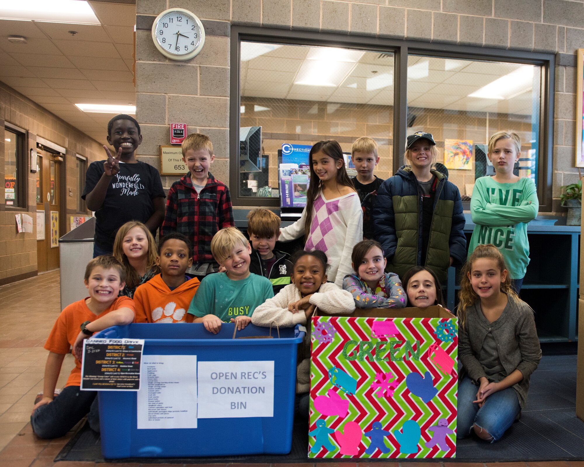Image of Youth Center children posing for a photo behind food drive donation bins, Dec. 13, 2018, at Mountain Home Air Force Base, Idaho. The Youth Center is holding a food drive to give canned and non-perishable food items to families in need. (U.S. Air Force photo by Senior Airman Alaysia Berry)