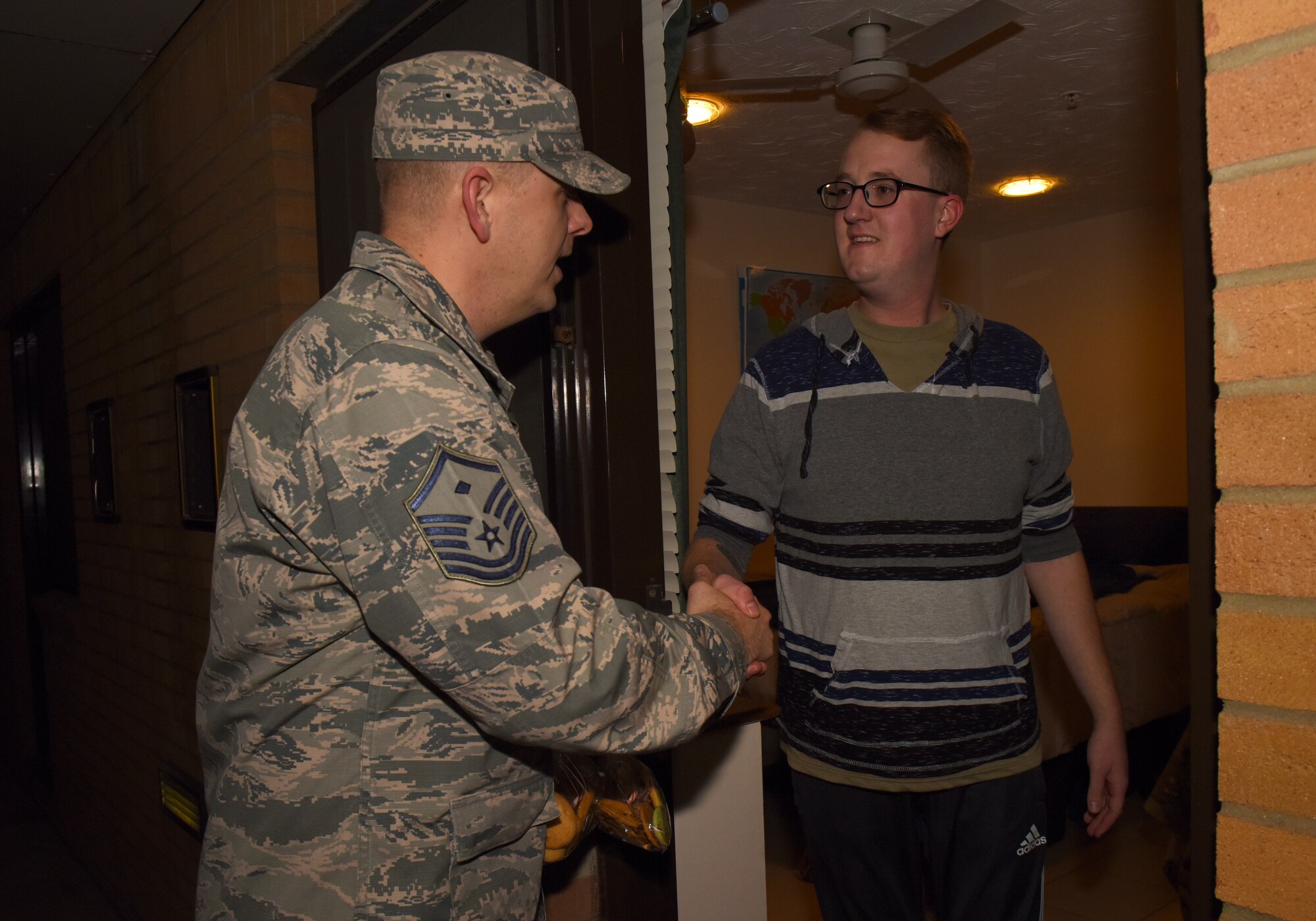 Airman 1st Class Robert McSweeney, a cyber-transport systems technician, assigned to the 48th Communications Squadron, receives cookies and holiday greetings from his first sergeant, Master Sgt. Jason Jenkins, during the Airman Cookie Drive at Royal Air Force Lakenheath, England, Dec. 12, 2018. The first sergeants went door-to-door handing out bags of cookies to their Airmen to spread some holiday cheer. (U.S. Air Force photo by Airman 1st Class Madeline Herzog)