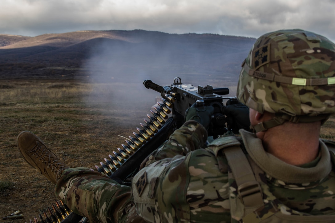 A soldier fires a machine gun across a large field.