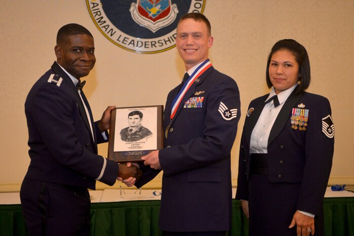Col. Terrence Adams (left), 628th Joint Base Charleston commander, and Master Sgt. Calantha Pickel (right), Airman Leadership Commandant, present Staff Sgt. Daniel Moore, 15th Airlift Squadron, a plaque for earning the John L. Levitow Award during the class 18/19-A Airman Leadership School Graduation at the Charleston Club here Dec. 13, 2018.