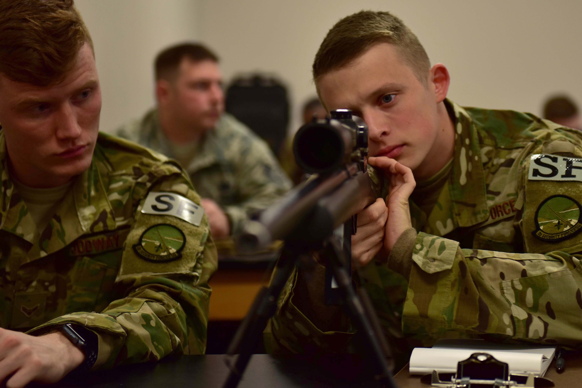 A man wearing the operational camouflage pattern uniform looks down the scope of a M24 sniper weapon system as a man wearing the OCP uniform watches him.