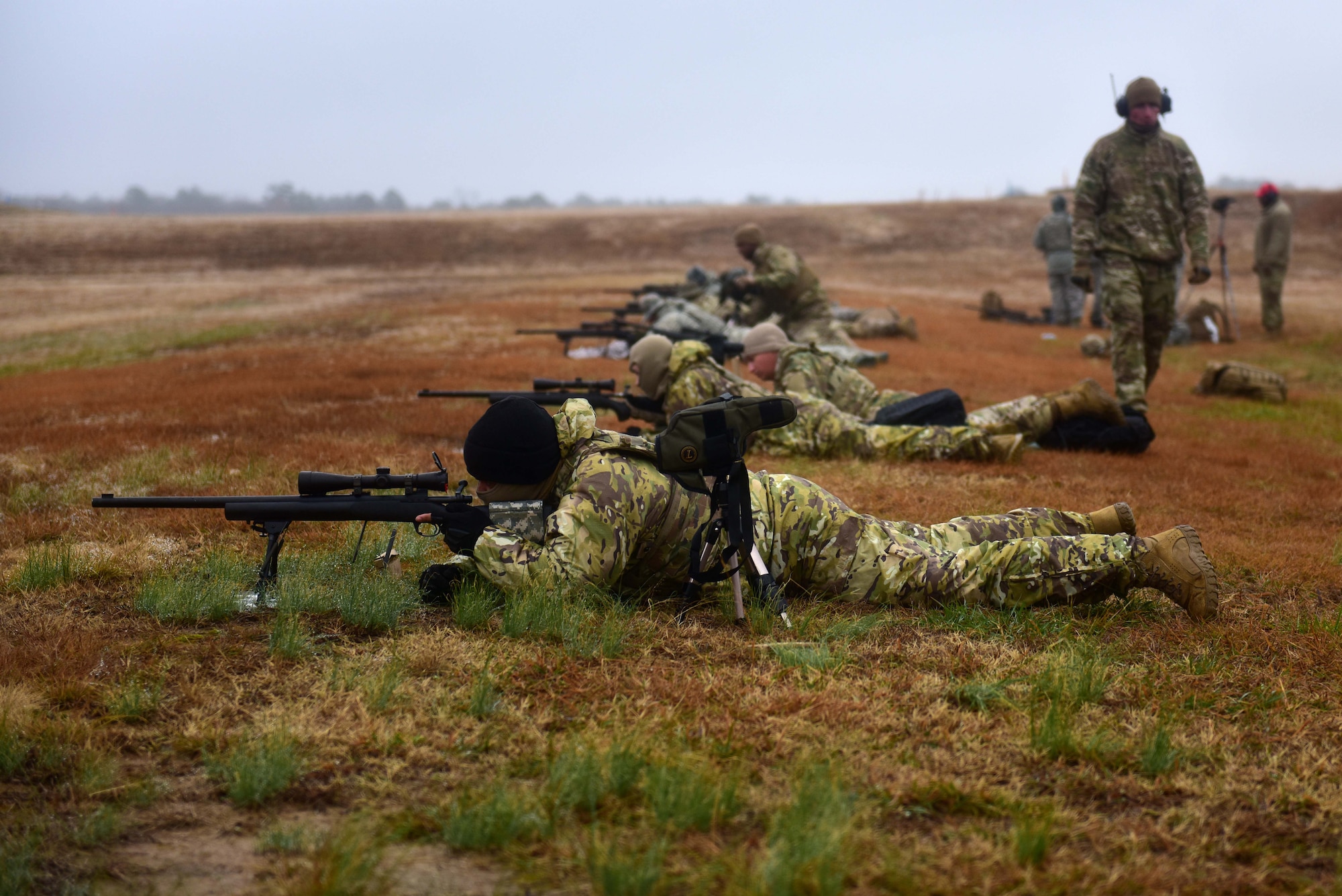 Men in military uniforms lay on ground looking down the scopes of M24 sniper weapon systems at a shooting range.