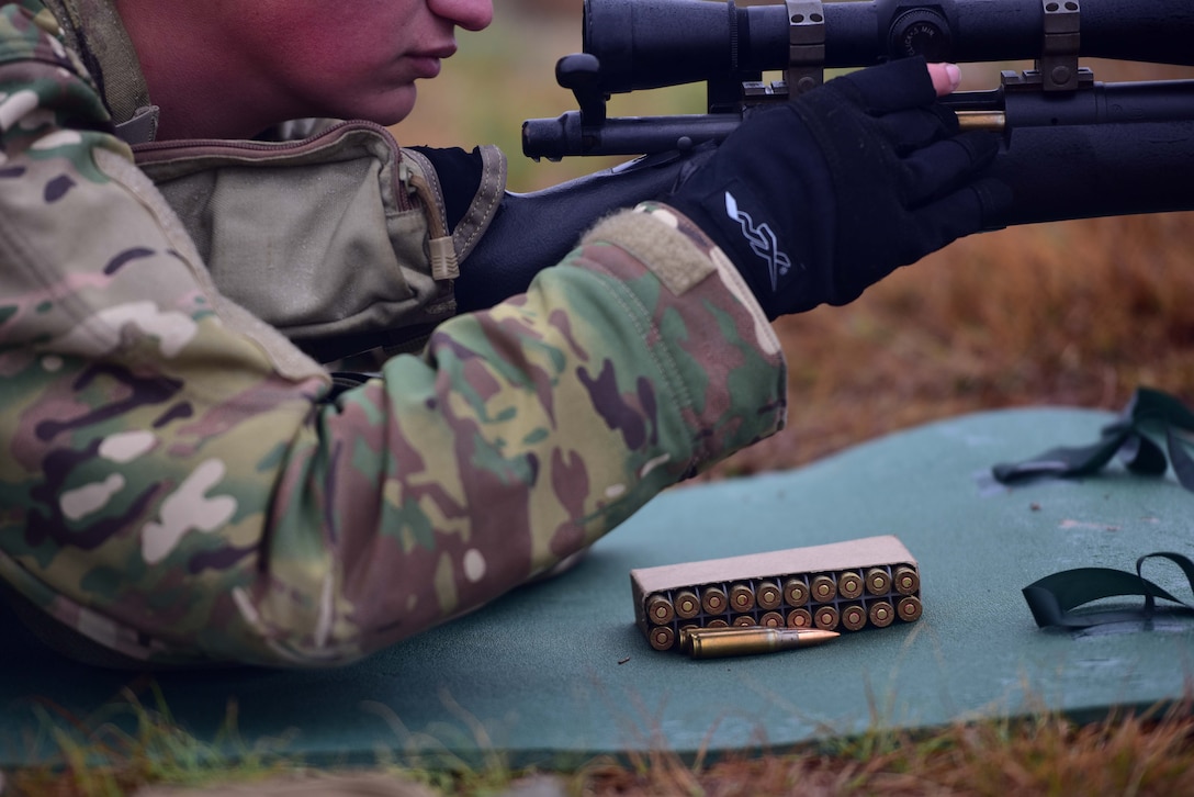 Bullets for a M24 sniper weapon system lay on a green mat as a man puts one into his M24.