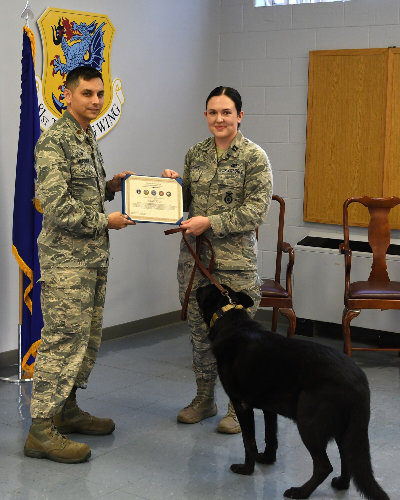 U.S. Air Force Maj. Jonathon Murray, left, 81st Security Forces Squadron commander, presents a certificate of appreciation to Bleck, 81st SFS military working dog, accepted by Capt. Samantha Giebel, right, 81st SFS operations officer, during a retirement ceremony at Keesler Air Force Base, Mississippi, Dec. 13, 2018. After serving eight years and working alongside 11 handlers during his career, he was adopted by Giebel. (U.S. Air Force photo by Airman 1st Class Suzie Plotnikov)