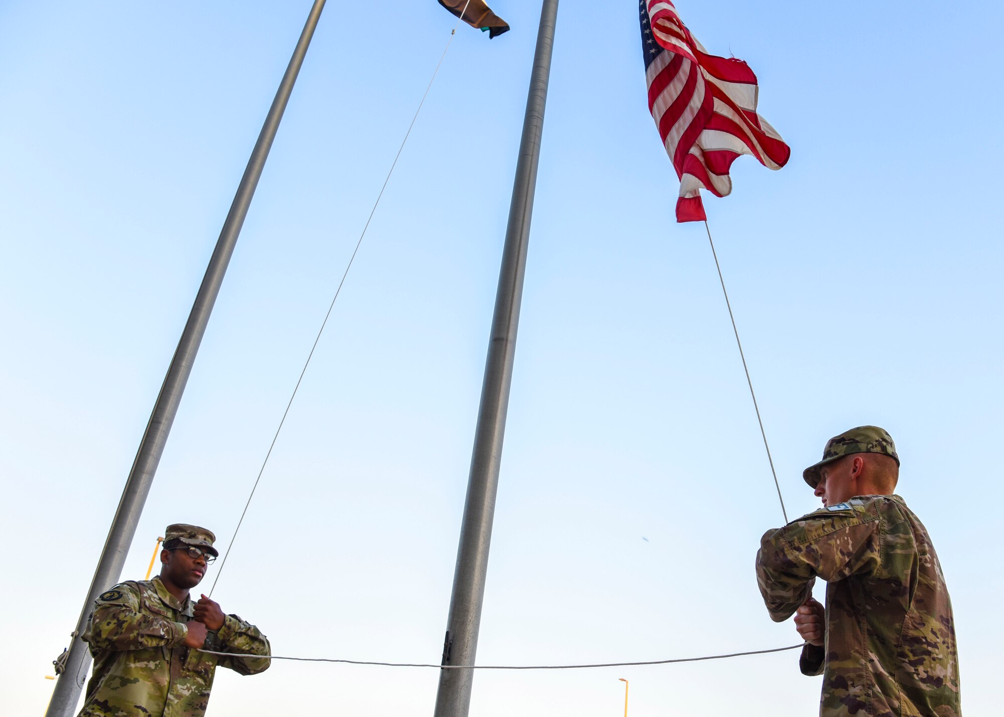 SrA William Rodriguez and SrA Johnathan Coble, 380th Expeditionary Security Forces Squadron, begin to lower the flag during a monthly retreat ceremony at Al Dhafra Air Base, United Arab Emirates, Dec. 7, 2018.