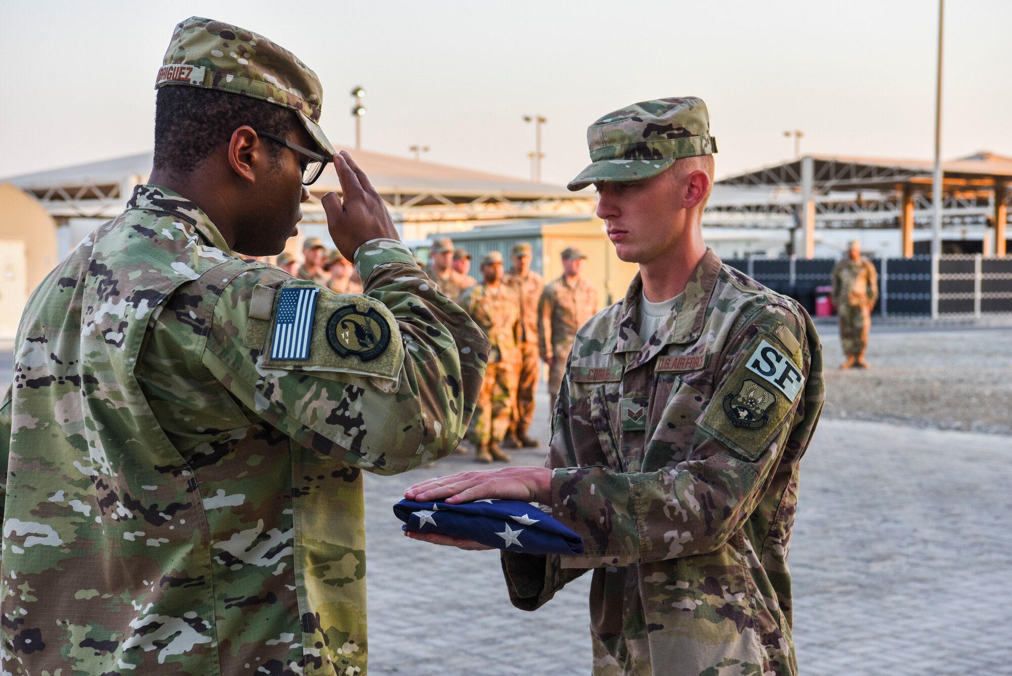 SrA William Rodriguez, 380th Expeditionary Security Forces Squadron, salutes the flag held by SrA Johnathan Coble, 380th Expeditionary Security Forces Squadron, during a monthly retreat ceremony at Al Dhafra Air Base, United Arab Emirates, Dec. 7, 2018.