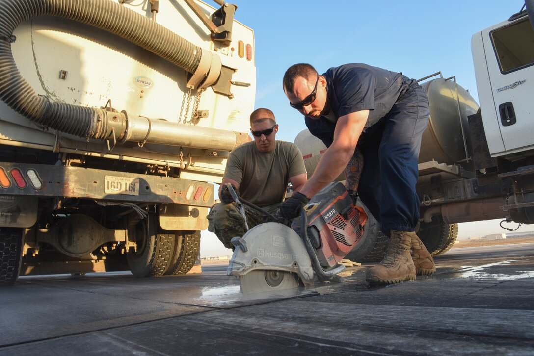 Senior Airman Charles Nelson, 380th Expeditionary Civil Engineering Squadron pavement and heavy equipment journeyman, uses water to enable Staff Sgt. Jesse Steinberg, 380th ECES pavement equipment journeyman, to cut a portion of the runway with a saw during runway repair at Al Dhafra Air Base, United Arab Emirates, Dec. 1, 2018.
