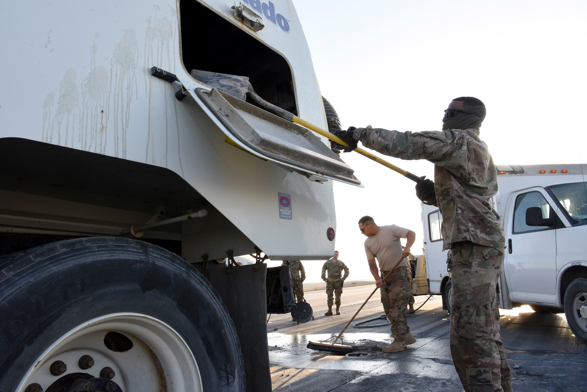 380th Expeditionary Civil Engineering Squadron pavement equipment journeymen Senior Airman Michael Horan (middle) sweeps debris while Airman 1st Class Kalvontae Smith (right), dumps it into the airfield sweeper during runway repairs at Al Dhafra Air Base, United Arab Emirates, Dec. 1, 2018.