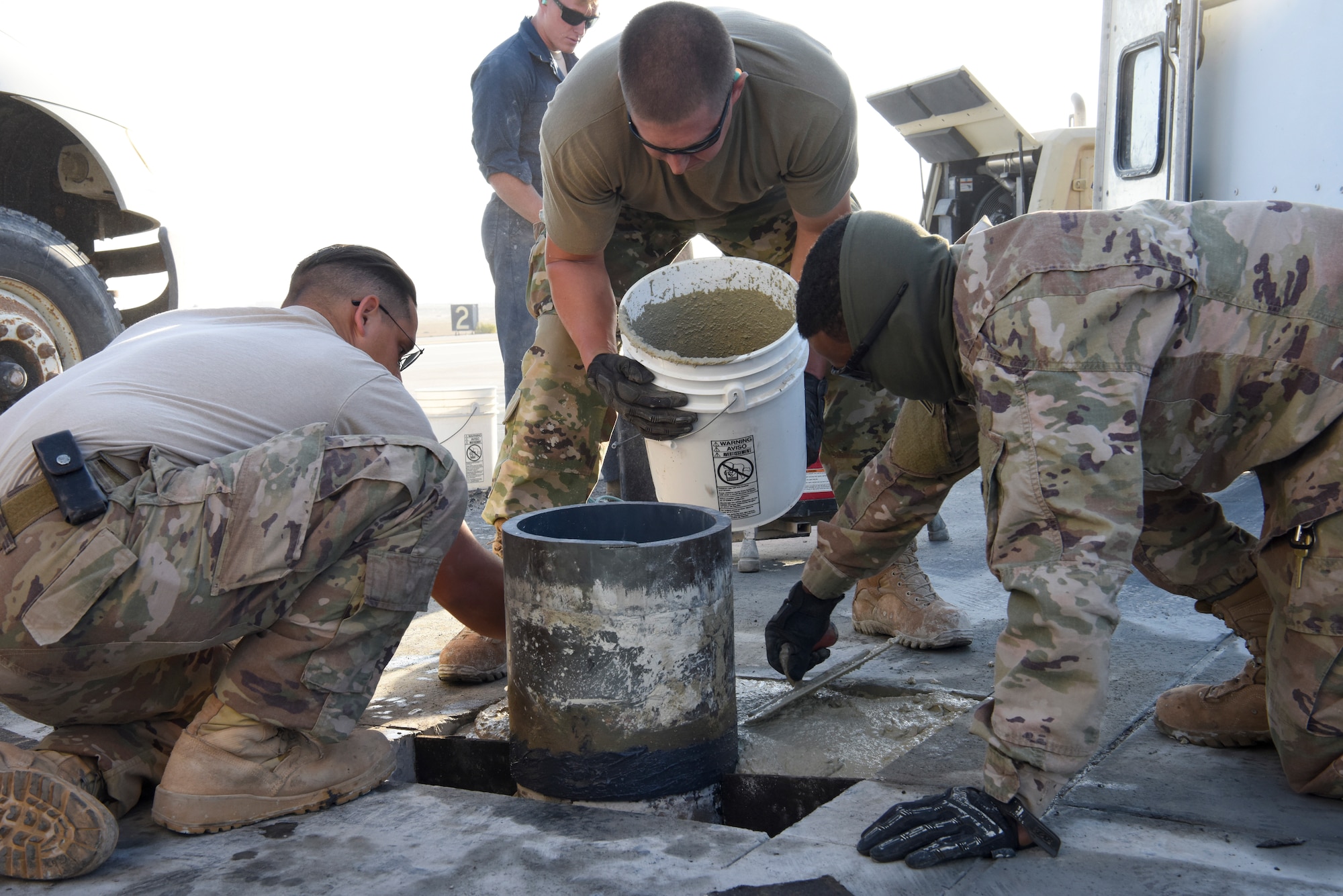 380th Expeditionary Civil Engineering Squadron pavement equipment journeymen Senior Airman Michael Horan (left) and Airman 1st Class Kalvontae Smith (right), smoothens the cement around the repaired area while Senior Airman Charles Nelson pours more into the hole during runway repairs at Al Dhafra Air Base, United Arab Emirates, Dec. 1, 2018.