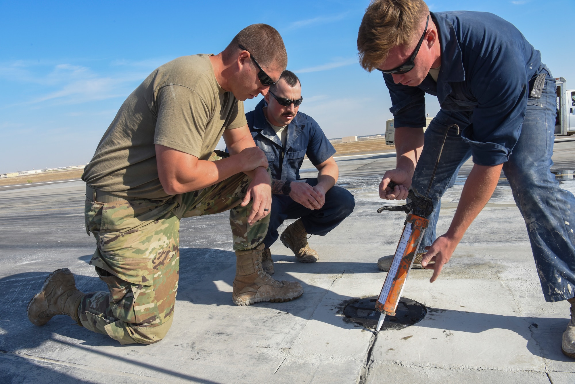 Senior Airman Charles Nelson (left) and Staff Sgt. Jesse Steinberg (middle) watches as Airman 1st Class Tyler Parker (right) seals the repaired runway area at Al Dhafra Air Base, United Arab Emirates, Dec. 1, 2018.
