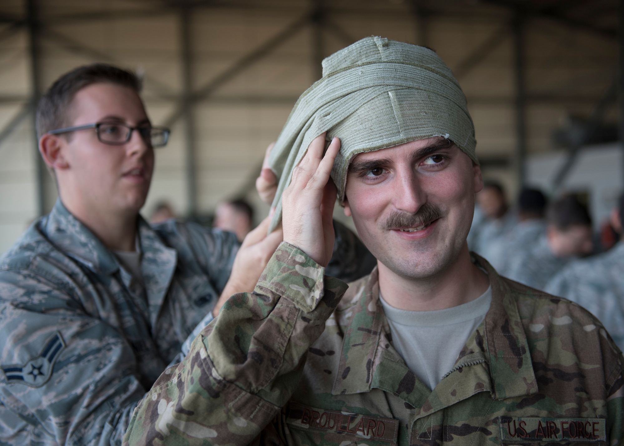 Two Airmen practice first aid bandaging on each other.