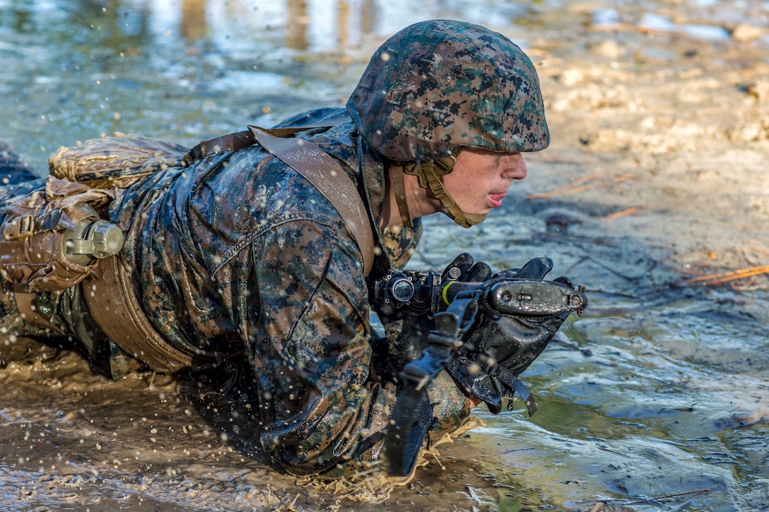 A Marine recruit crawls through water.