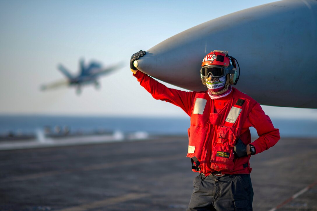 A sailor stands while holding on to an airplane nose cone.