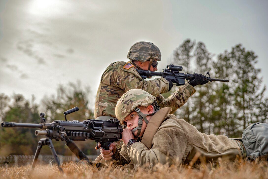 Two soldiers aim down sights in a field.