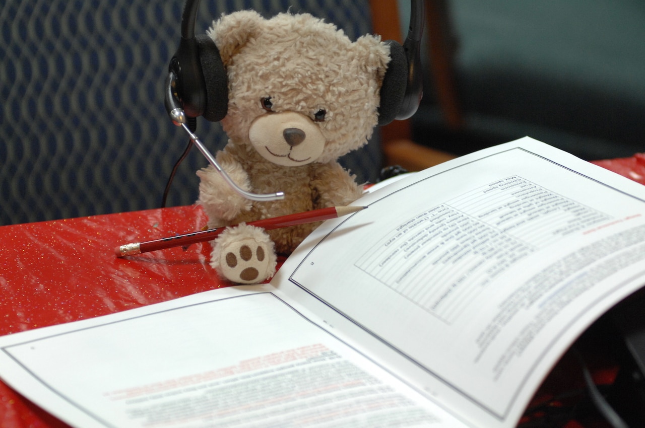A teddy bear wears a headset while reading a pamphlet.