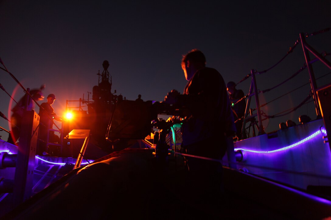 Service members work on board a military ship at night.