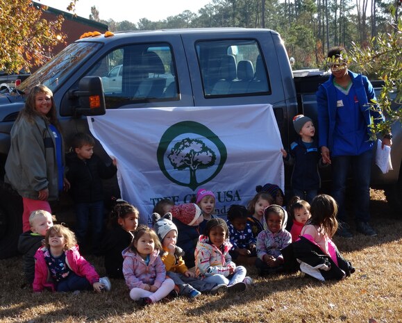 Children pose for a group picture with a Tree City USA banner after assisting natural resources staff plant a Live Oak tree at the Joint Base Charleston Naval Weapons Station Child Development Center during the base’s Arbor Day celebration, held annually on Dec. 7.